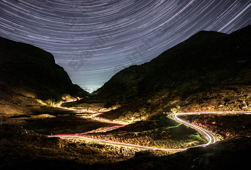 Gap of Dunoe Star Trails 
 "Star Trails in The Gap of Dunloe"
Taken on a Cold Night in early January. I took a five minute long photograph to expose for the foreground. I was fortunate that a car drove into frame as I was taking the shot. The light trail along the road is the car driving along the road to Kate Kearneys over a five minute period.
I then took 250 shorter photographs of the night sky over a 90 minute period. Each of these photos shows the stars have moved slightly in their position. You then blend all of these together to give the impression of movement across the night sky.
So what you are actually seeing in effect is the earth's rotation through the solar system in a 90-110 minute period in relation to the stars.